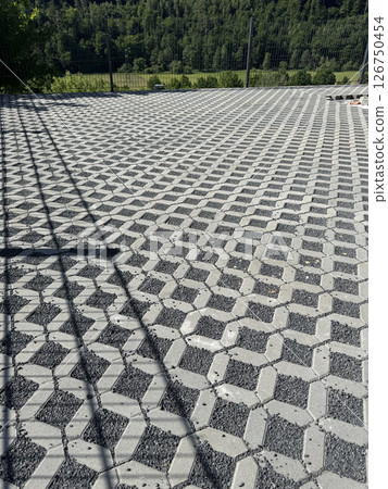 A wide view of geometric concrete pavers arranged in a seamless pattern. These pavers are set outdoors, bordered by a lush green forest, creating an elegant and durable surface. 126750454