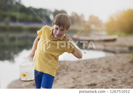 A little boy has caught a goldfish and is carrying it in a glass jar.Happy fishermen. A little boy has caught a goldfish and is carrying it in a glass jar.Happy fishermen. 126751052