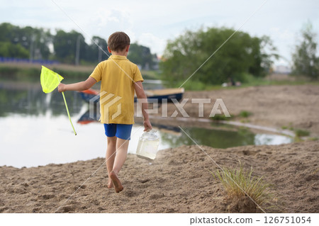 A little boy with a fishing net walks along the shore of the lake. 126751054
