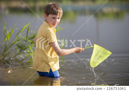 A little boy with a butterfly net catches fry in the lake. 126751061