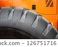 A CloseUp Image Featuring a Heavy Machinery Tire Against a Bright Orange Background 126751716