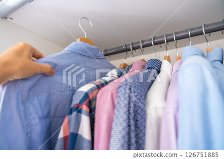 Male hand selecting a shirt from a wardrobe full of clothes on wooden hangers. Concept of clothing choice, daily routine and personal style. Male hand selecting a shirt from a wardrobe full of clothes on wooden hangers. Concept of clothing choice, daily routine and personal style. 126751885