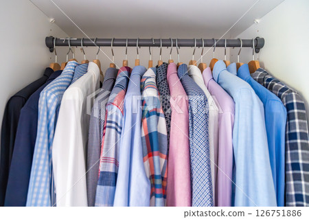 Neatly arranged men shirts hanging on wooden hangers in wardrobe. Minimalist clothing organization and classic male fashion concept Neatly arranged men shirts hanging on wooden hangers in wardrobe. Minimalist clothing organization and classic male fashion concept 126751886