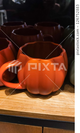 Orange pumpkin shaped mugs resting on wooden shelf Orange pumpkin shaped mugs resting on wooden shelf 126752883