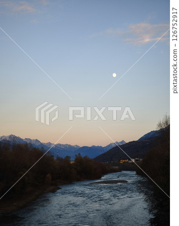 Moonlit river winding through mountain valley, snow peaks glimmering against dark sky, casting soft light on calm waters Moonlit river winding through mountain valley, snow peaks glimmering against dark sky, casting soft light on calm waters 126752917