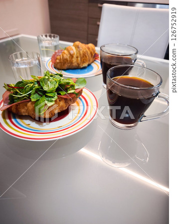 Crisp croissants, steaming coffee on glass surface, warm morning scene with vibrant tableware and refreshing water glasses Crisp croissants, steaming coffee on glass surface, warm morning scene with vibrant tableware and refreshing water glasses 126752919