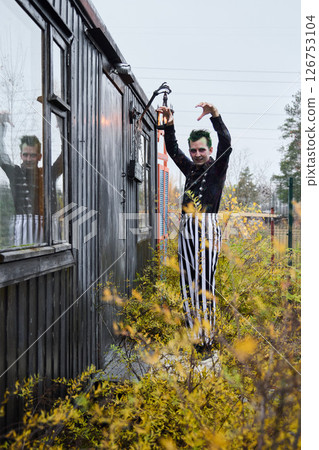 A mysterious performer in striped attire stands by an abandoned building, evoking curiosity A mysterious performer in striped attire stands by an abandoned building, evoking curiosity 126753104