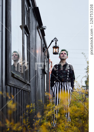 A Stylish Individual Posing Confidently Near a Vintage Cabin in a Beautiful Setting 126753108