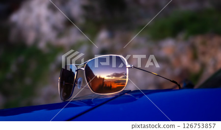 Pair of sunglasses reflecting a sunset on the beach. Relaxed summer tourism concept Pair of sunglasses reflecting a sunset on the beach. Relaxed summer tourism concept 126753857
