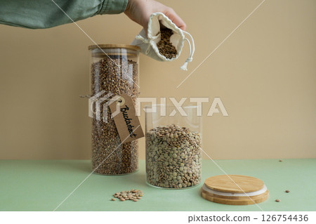 Unrecognizable woman refill Refillable glass jar with raw buckwheat and green lentil porridge in cotton bag. Product format eco-friendly living. Filling reusable container Whole spelt grain species Unrecognizable woman refill Refillable glass jar with raw buckwheat and green lentil porridge in cotton bag. Product format eco-friendly living. Filling reusable container Whole spelt grain species 126754436