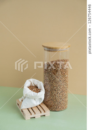 Refillable glass jar with raw buckwheat porridge and cotton bag. Copy space Refill product format eco-friendly living. Filling reusable container Whole spelt grain species. High protein fiber-rich 126754446