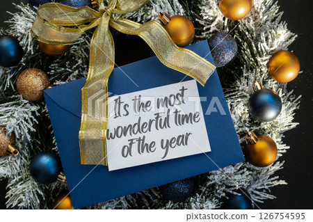 Greeting card with IT'S THE MOST WONDERFUL TIME OF THE YEAR text on handmade Christmas wreath. Festive mood new year celebration. Postcard decoration decor 126754595