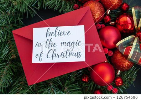 BELIEVE IN THE MAGIC OF CHRISTMAS text on postcard with red envelope on handmade Christmas wreath. Zero waste eco-friendly Christmas. Sustainable greeting card 126754596