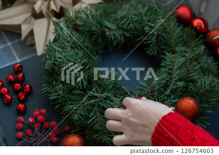 Step by step instruction of making handmade Christmas wreath made of festive decorations in red color. Female hands creating craft homemade decor. New year celebration. Winter holidays 126754603