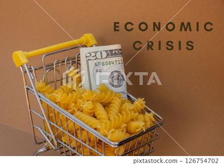ECONOMIC CRISIS text against Shopping trolley cart Filled With Pasta with 20 US dollar paper money banknote on Beige background. Food and groceries shopping price increase, Rising food cost food 126754702