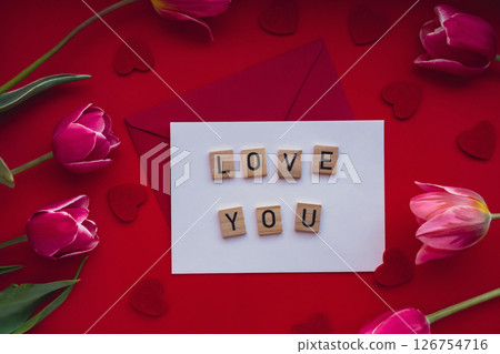 LOVE YOU text message on envelope with beautiful pink tulip bouquet on red background. Template mock up for holiday greeting card. Love romance Valentines day Top view Flat lay Feminine concept 126754716