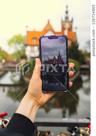 Female traveler in historical places courtyard of landmark and shoots short video on phone. Tourist photographs historic place on sunny day in Gdansk Poland. Unrecognizable woman Tourism and blogging Female traveler in historical places courtyard of landmark and shoots short video on phone. Tourist photographs historic place on sunny day in Gdansk Poland. Unrecognizable woman Tourism and blogging 126754805