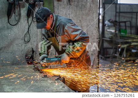 Metalworker Grinding Steel in Industrial Workshop with Bright Flying Sparks Metalworker Grinding Steel in Industrial Workshop with Bright Flying Sparks 126755261