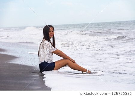 Happy woman sitting on the beach with waves in the background Happy woman sitting on the beach with waves in the background 126755585