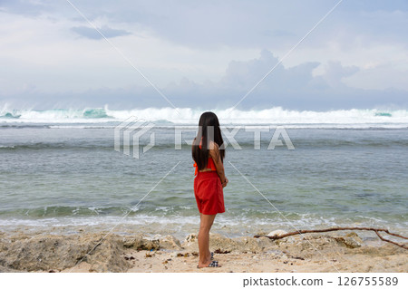 A young lonely woman stands on the shore of a stormy sea and looks into the distance at the waves A young lonely woman stands on the shore of a stormy sea and looks into the distance at the waves 126755589