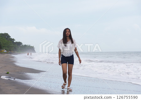 young woman walking alone on the beach near the sea waves 126755590