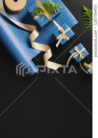 Flat composition with blue gifts with gold ribbons, brown paper tags, green thuja branches on black background. Space for your text. 126756455
