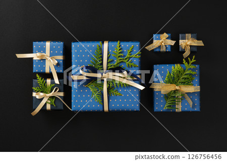 Neatly arranged gift boxes wrapped in blue polka dot and navy paper are decorated with shiny gold and cream ribbons, accented by fresh green thuja sprigs. Neatly arranged gift boxes wrapped in blue polka dot and navy paper are decorated with shiny gold and cream ribbons, accented by fresh green thuja sprigs. 126756456