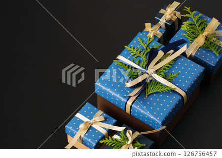 Selective focus wrapped gifts decorated with blue polka dot paper, gold ribbons and sprigs of fresh greenery on a black background. Space for your text Selective focus wrapped gifts decorated with blue polka dot paper, gold ribbons and sprigs of fresh greenery on a black background. Space for your text 126756457