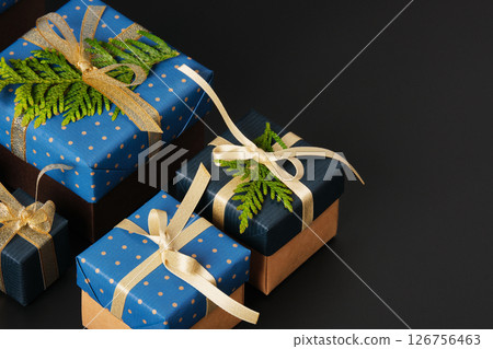 Selective focus wrapped gifts decorated with blue polka dot paper, gold ribbons and sprigs of fresh greenery on a black background. Space for your text 126756463