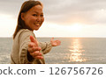 A Radiantly Joyful Woman Embracing the Beautiful Golden Sunset by the Calm Ocean Waves at Dusk 126756726