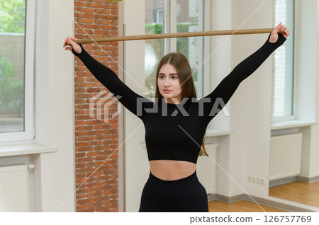 Young woman stretching with wooden stick in fitness studio. 126757769