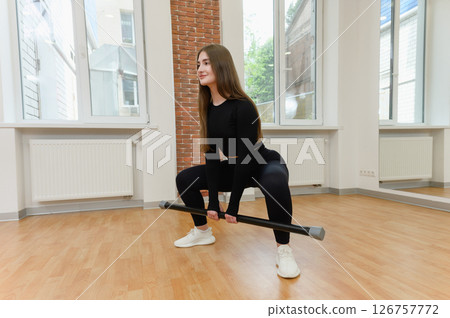 Young woman squatting with fitness bar in gym studio. 126757772