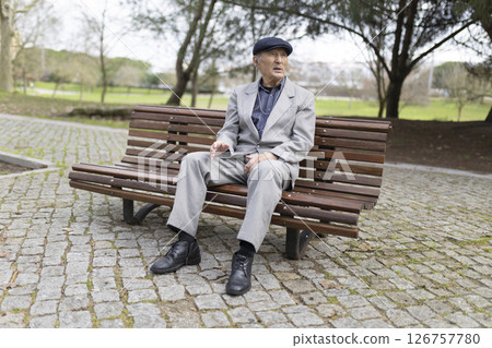 Elegant senior man sitting on bench in park talking and gesturing 126757780