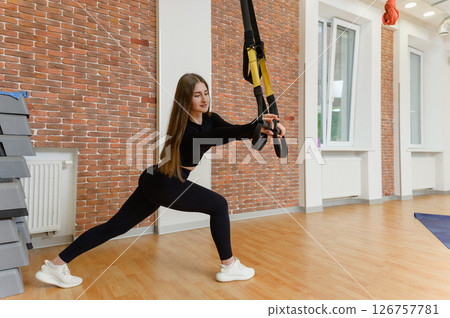 Young woman in sports clothing training with trx fitness straps in the gym. Young woman in sports clothing training with trx fitness straps in the gym. 126757781