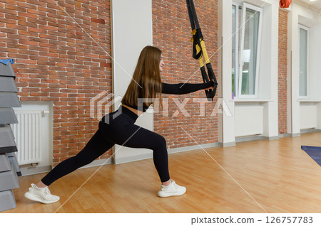 Young woman in sports clothing training with trx fitness straps in the gym. 126757783