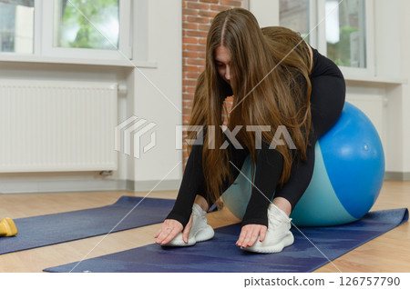 Woman stretching forward while seated on fitness ball. 126757790