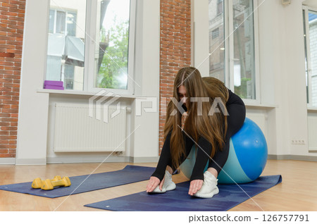 Woman stretching forward while seated on fitness ball. Woman stretching forward while seated on fitness ball. 126757791