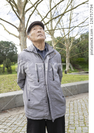 Elderly asian man listening to music in park looking up 126757794