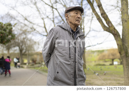 Elderly asian man listening music with earphones while walking in park 126757800