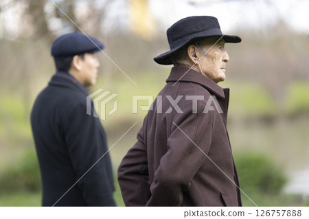 Two senior men wearing hats standing in park looking away 126757888