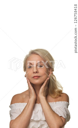 Graceful older woman presses hands to jawline, massaging face against white background, showing confident aging and daily facial care Graceful older woman presses hands to jawline, massaging face against white background, showing confident aging and daily facial care 126758418
