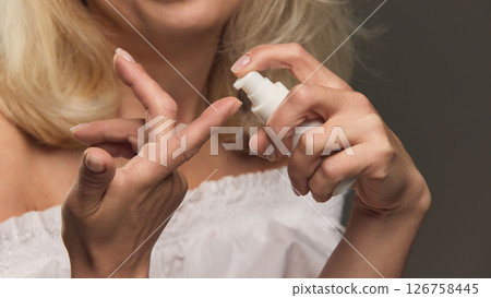 Close-up portrait of mature hands pressing skincare pump onto finger with care against dark studio background Close-up portrait of mature hands pressing skincare pump onto finger with care against dark studio background 126758445