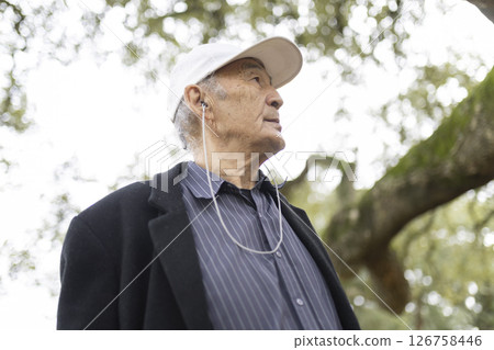 Senior man wearing earphones listening music in park 126758446