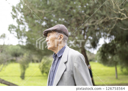 Elderly man listening music with earphones while walking in park Elderly man listening music with earphones while walking in park 126758564