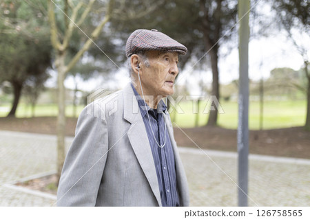Elderly gentleman listening music walking in park Elderly gentleman listening music walking in park 126758565