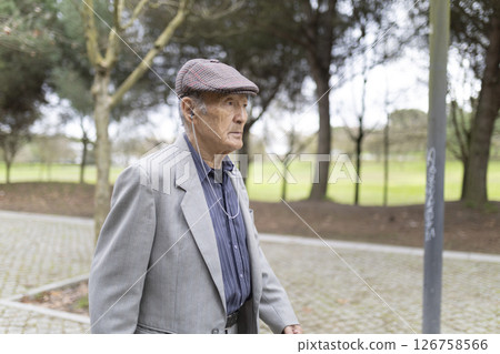 Elderly gentleman listening to music while walking in park 126758566