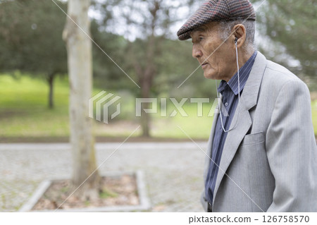 Elderly man listening to music while walking in park Elderly man listening to music while walking in park 126758570