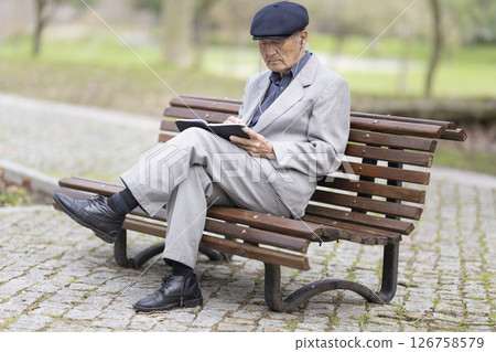Elderly writer taking notes in notebook while sitting on park bench Elderly writer taking notes in notebook while sitting on park bench 126758579