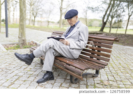 Elderly asian man sitting on bench writing in notebook in park Elderly asian man sitting on bench writing in notebook in park 126758599