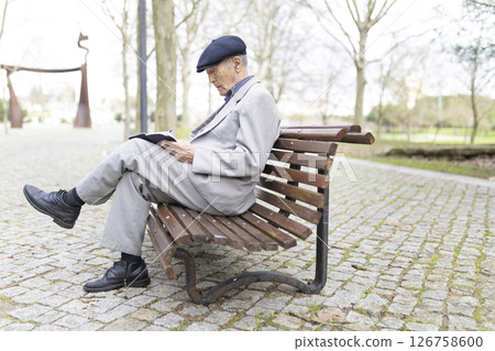 Senior professor writing notes while sitting on bench in park Senior professor writing notes while sitting on bench in park 126758600